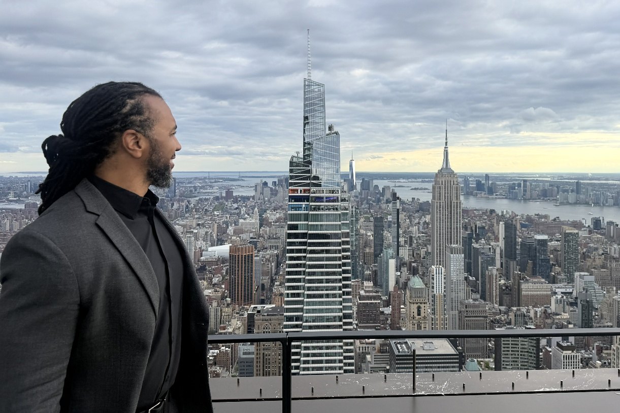 Usama Young in a gray blazer looking out over the Manhattan skyline